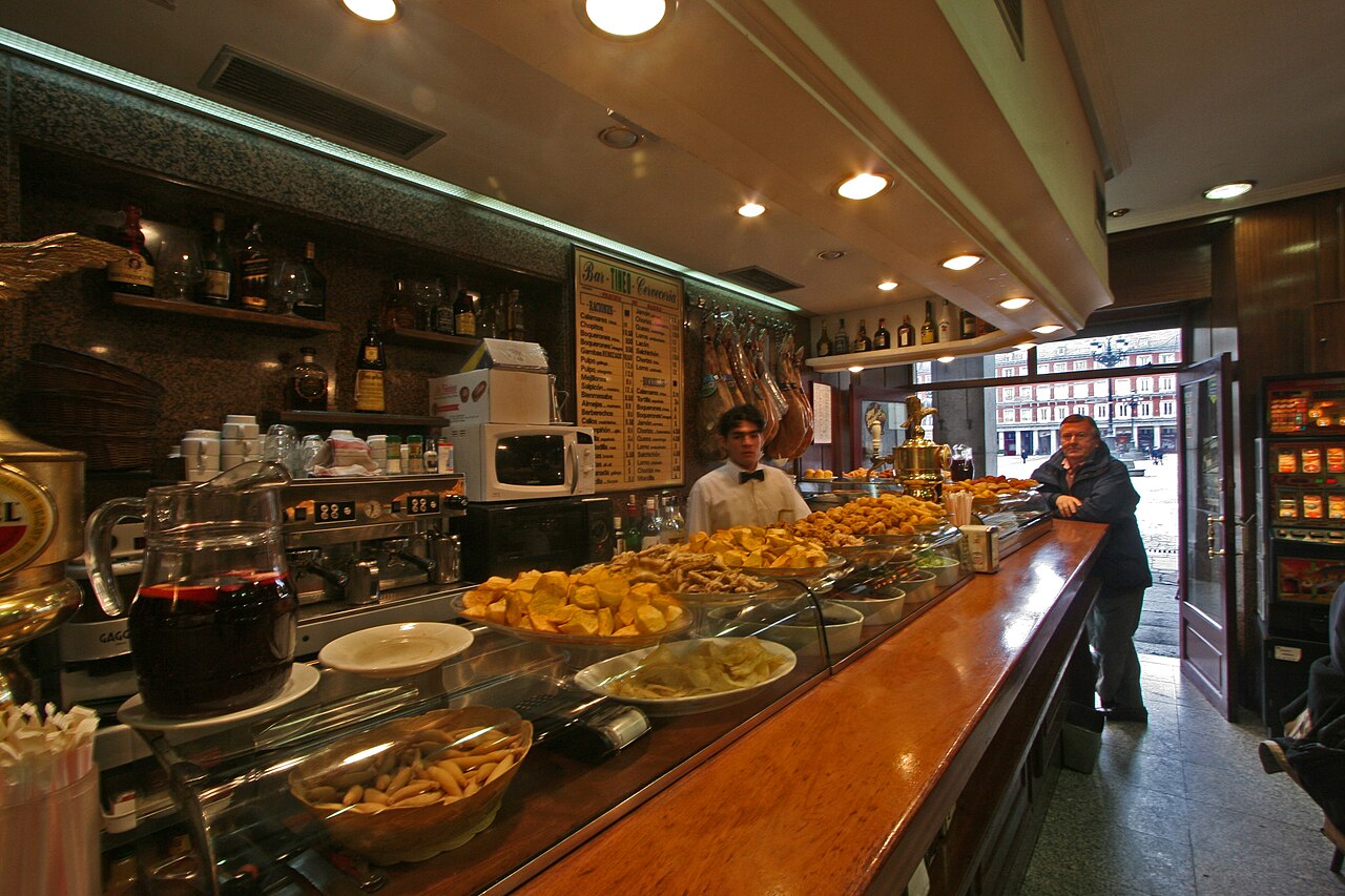 A busy tapas bar counter near Plaza Mayor in Madrid, dishes lined up under glass